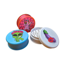 Three colourful Magic Leaf "Print Collection" plastic grinders with alien, unicorn, and lipstick designs on a white background.